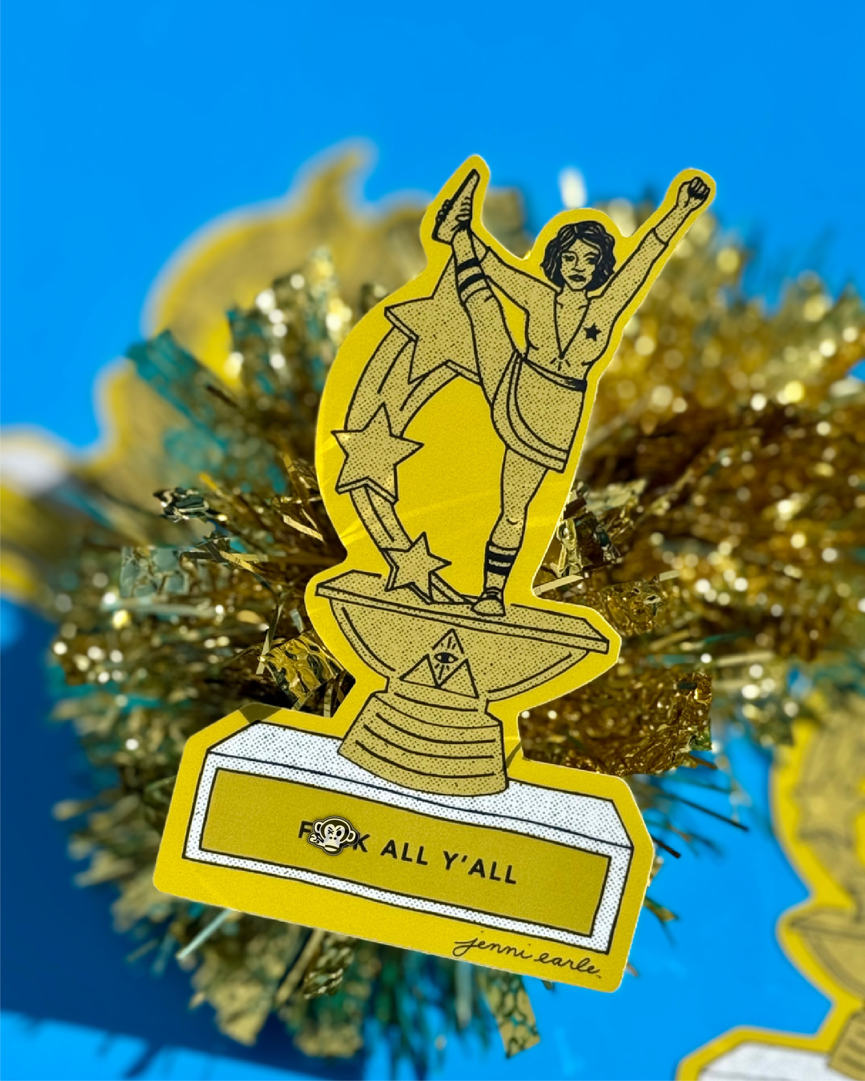 A die cut sticker featuring a woman triumphantly standing on top of a trophy, celebrating achievement and success with a plaque saying "Fuck All Y'All".