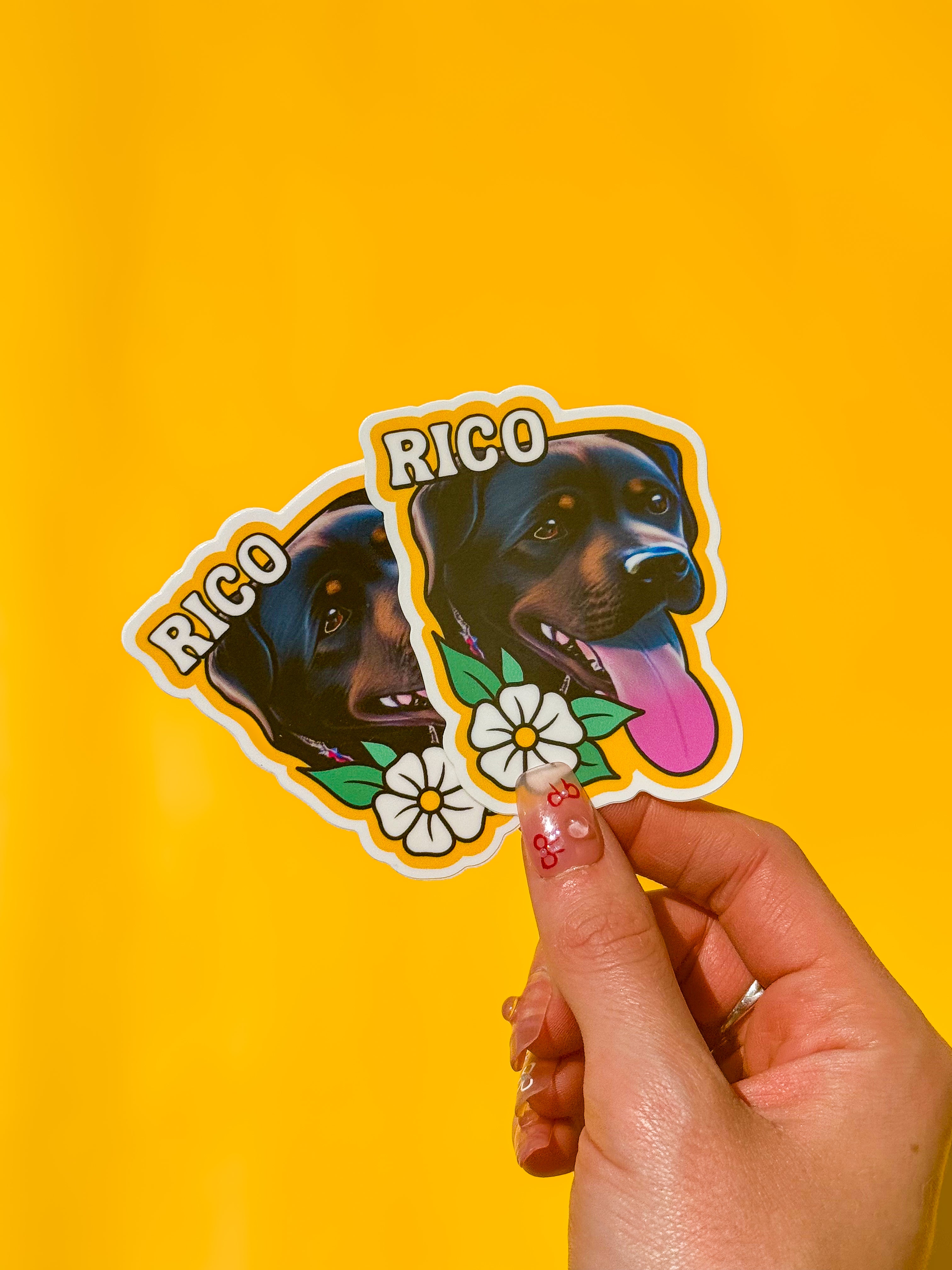 Example of a custom die cut sticker featuring a black and tan dog named Rico, decorated with white flowers and bold text on a bright yellow background.