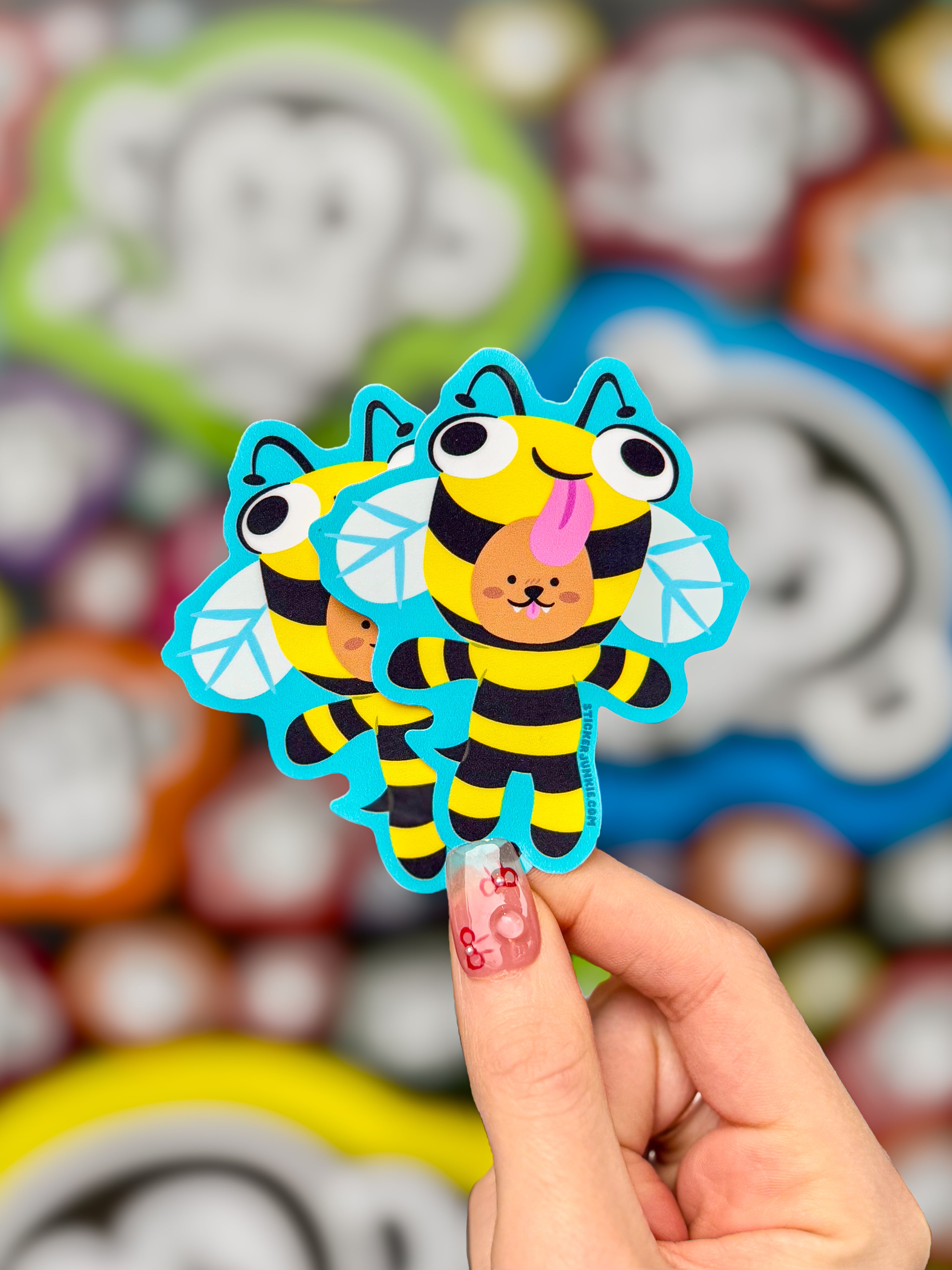 A hand holds two die cut stickers featuring a monkey in a bee costume, showcasing colorful design.