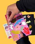 Hand holding a colorful notebook with abstract designs on a yellow background